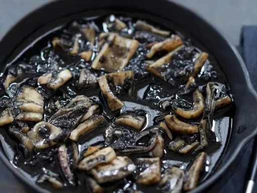 Calamares en su tinta, un plato oscuro y sabroso, servido en una sartén de hierro fundido.