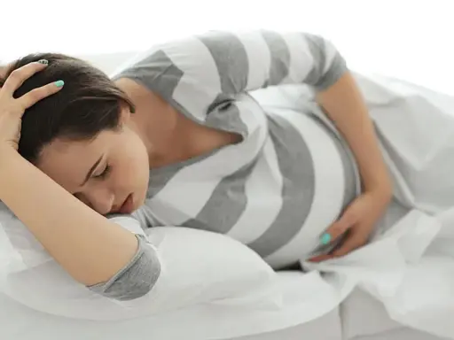 Schwangere Frau liegt auf dem Bett, hält sich den Kopf und fragt sich: "Vorwehen, wie lange noch bis zur Geburt?