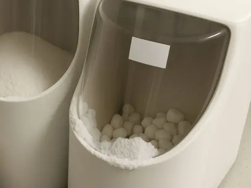 Deux bacs blancs remplis de sel pour adoucisseur d'eau, l'un en poudre, l'autre en pastilles.