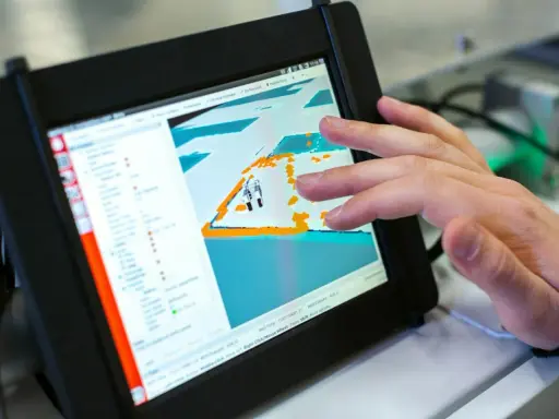 Ein Finger tippt auf ein Tablet, das eine 3D-Ansicht mit einem Roboter zeigt. Die dji app windows wird zur Steuerung genutzt.