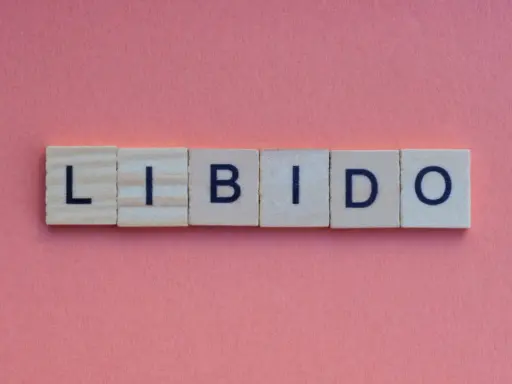 Słowa "LIBIDO" ułożone z klocków na różowym tle. Temat: spadek libido u mężczyzn po 30.