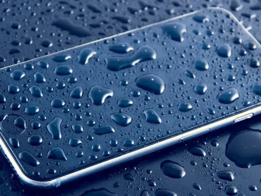 Smartfon pokryty kroplami wody, podkreślający jego wodoodporność IP.