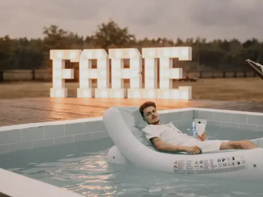 Relaks przy basenie z drinkiem, wielkie litery "FARTE" w tle. Idealny pomysł, jak zorganizować wieczór kawalerski.