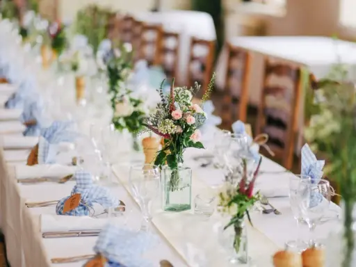 Disposition des couverts à la française sur une longue table dressée pour un événement, avec des fleurs sauvages et des serviettes à carreaux bleus.