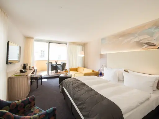 Modernes Hotelzimmer mit Doppelbett, Sofa, Schreibtisch und Balkon.