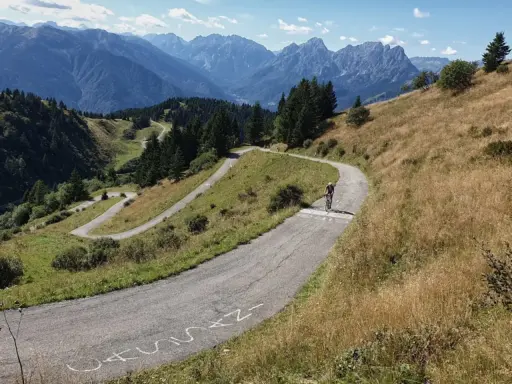 Radfahrer kämpft sich die Serpentinen des Monte Zoncolan hoch. Majestätische Berge im Hintergrund.