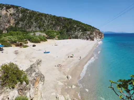 Malownicza plaża Gjipe z turkusową wodą, skalistymi klifami i kilkoma turystami relaksującymi się na piasku.