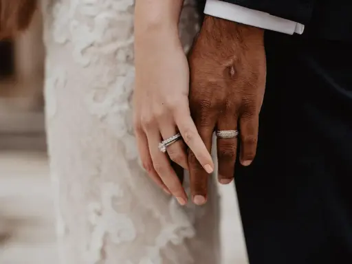 Manos entrelazadas, mostrando el anillo de casada en la mano izquierda de ella y el de él en la derecha.
