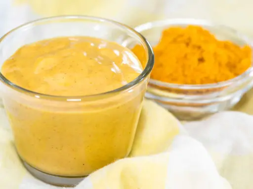 Sauce curry onctueuse dans un verre, avec une coupelle de poudre de curcuma à côté. Parfait pour relever vos plats.