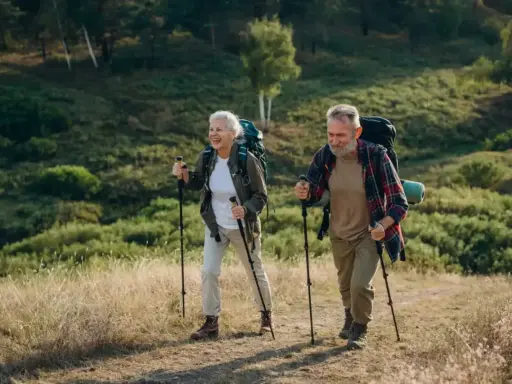 Uśmiechnięta para seniorów z plecakami przemierza leśny szlak, ucząc się, jak chodzić z kijkami.
