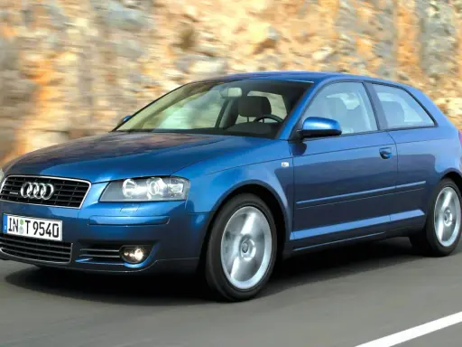 Niebieskie Audi A3 8P w ruchu, z widocznymi przednimi żarówkami, pędzi po drodze wśród skalistych zboczy.