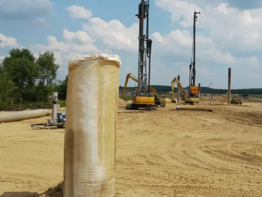 Construcción en terreno arenoso, con maquinaria pesada y tuberías. Se aprecian varios tipos de suelos blandos, listos para la obra.