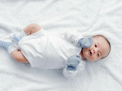 Dolce neonato nel suo primo mese, sdraiato su un soffice telo bianco, con calzini azzurri e guantini.