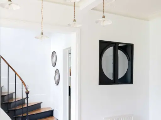 Entrée lumineuse avec escalier aux marches en bois et contremarches noires. Quelle couleur pour une entrée avec escalier ? Ici, le blanc éclatant met en valeur le design.