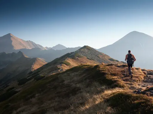 Wędrowiec na grani Tatr, idealne tatry szlaki dla średnio zaawansowanych. Słońce oświetla trawiaste zbocza i skaliste szczyty.