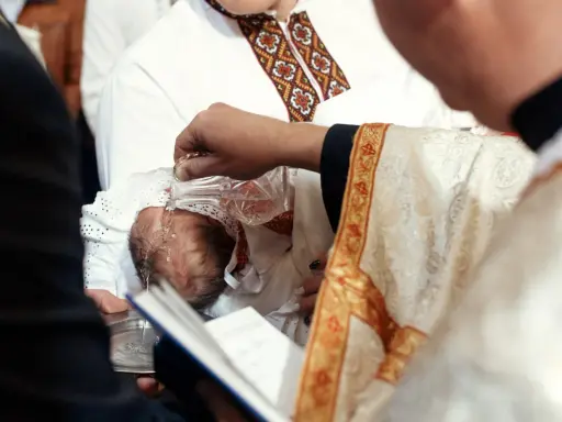 Chrzestni słuchają słów kapłana, gdy ten polewa wodą głowę niemowlęcia.