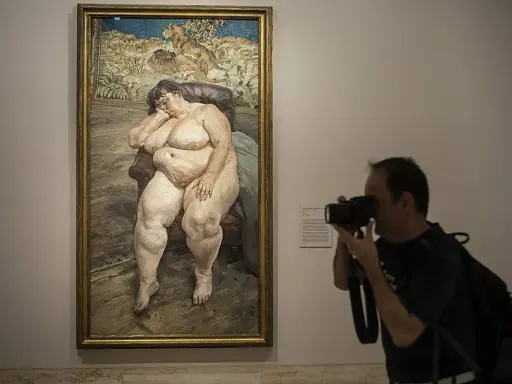 Un hombre fotografía un cuadro de **lucian freud desnudos**, una figura sentada en un sillón, capturando la intimidad de la obra.