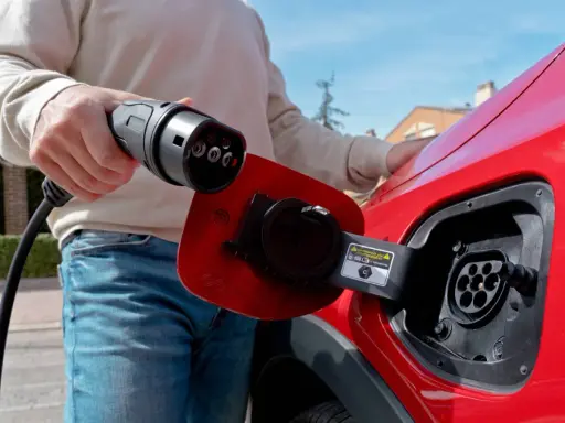 Persona desconectando el cargador de un coche eléctrico rojo.