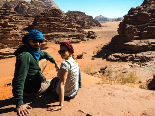 Para w turbanach odpoczywa na piasku, podziwiając skaliste krajobrazy pustyni Wadi Rum.