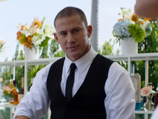 Channing Tatum som bartender i en film. Han ser ut att vara redo att servera drinkar med blommor och flaskor i bakgrunden.