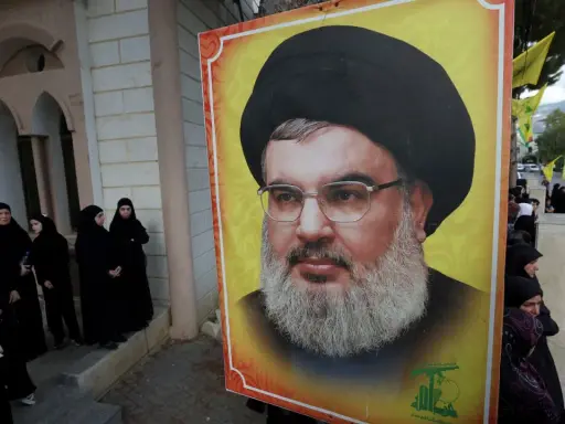 Wielki portret Hassana Nasrallaha, lidera Hezbollah, obok grupy kobiet w czarnych hidżabach.