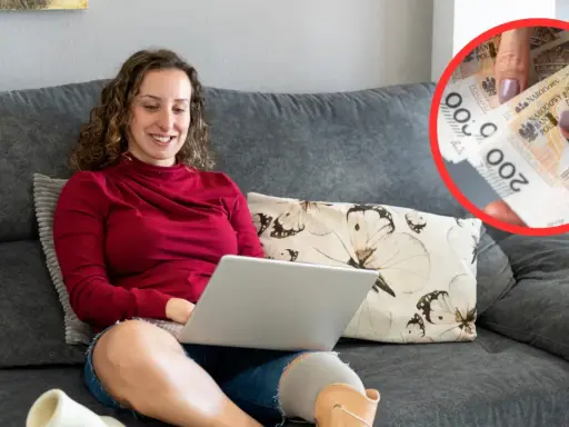 Kobieta z protezą nogi korzysta z laptopa. W tle widać dłonie trzymające polskie banknoty 200 zł, co może symbolizować wsparcie finansowe, np. związane z symbolem niepełnosprawności 05-r co przysługuje.
