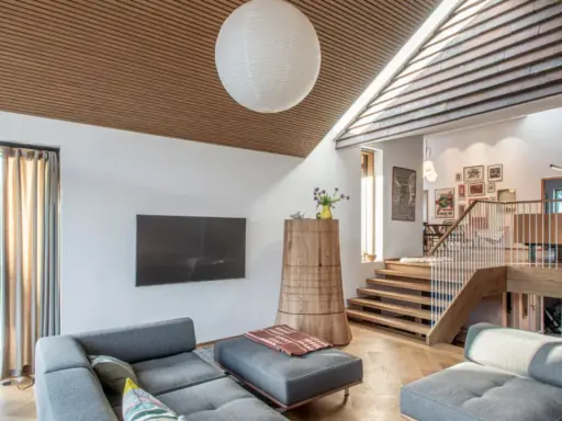 Modernes Wohnzimmer mit grauem Sofa und einem interessanten **split level** Design, das durch eine Holztreppe und einen offenen Wohnbereich gekennzeichnet ist.