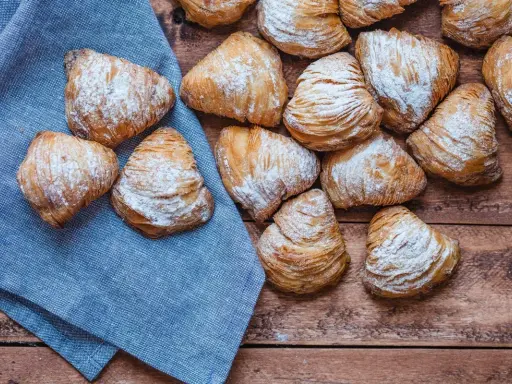 Sfogliatelle, un delizioso cibo tipico napoletano, cosparse di zucchero a velo su un tavolo di legno e un tovagliolo blu.