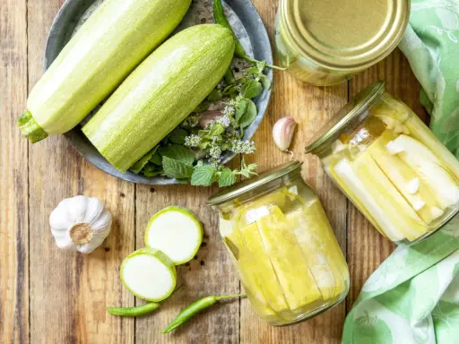 Zucchini haltbar machen: Frische Zucchini, Knoblauch, Chili und Kräuter für die Konservierung in Gläsern.