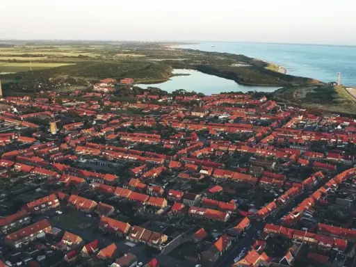 Luftaufnahme einer Küstenstadt in den Niederlanden mit roten Dächern, einem Leuchtturm und dem Meer. Drohnenaufnahmen zeigen die Schönheit der Niederlande.