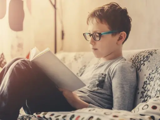 Bambino con occhiali legge un libro, concentrato su come imparare una poesia a memoria.