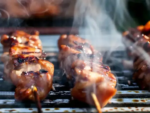 Aromatyczne yakitori skwierczy na grillu, otoczone kłębuszkami dymu.