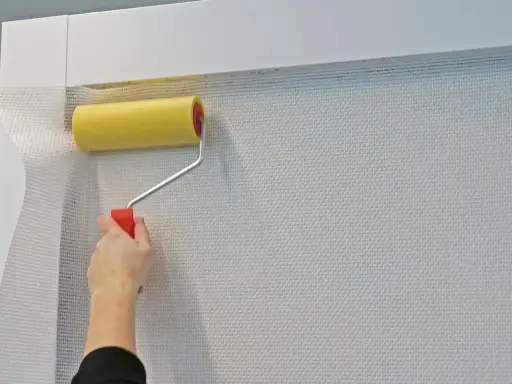 Mit einem gelben Farbroller wird eine weiße Tapete spachteln.