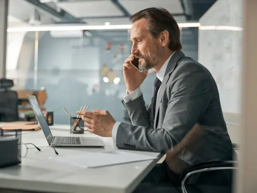Mężczyzna w garniturze rozmawia przez telefon, pracując przy laptopie. To typowy dzień w pracy, nawet dla samego CEO.