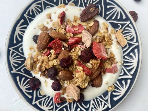Schüssel mit Joghurt, garniert mit knusprigem Müsli, Mandeln, gefriergetrockneten Erdbeeren und Blaubeeren. Perfekt für gesunde Frühstücks-Granola-Rezepte.