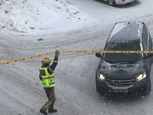 En räddningsarbetare spärrar av ett område med band. Snö faller och täcker marken och en bil. Kanske har något ruttnande material hittats.