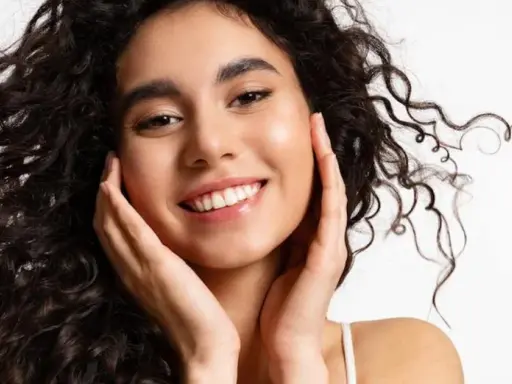 Sonrisa radiante con un toque de strawberry makeup, cabello rizado oscuro y piel luminosa.