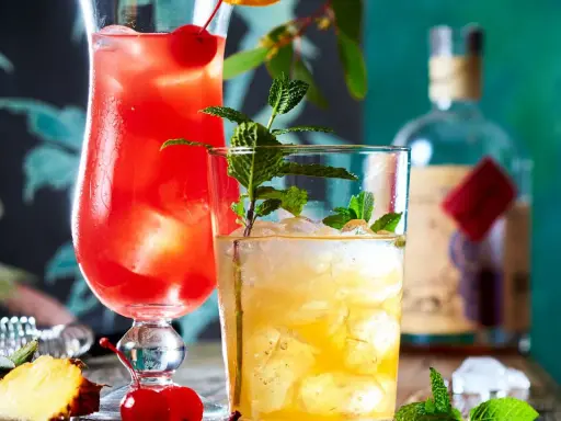 Zwei erfrischende Cocktails, einer rot, der andere gelb, mit Minze und Früchten. Ein **Cocktail mit Bier**-Mix? Vielleicht.