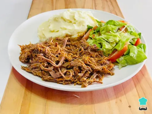 Plato de carne mechada jugosa, puré de papas cremoso y ensalada fresca de lechuga y tomate.