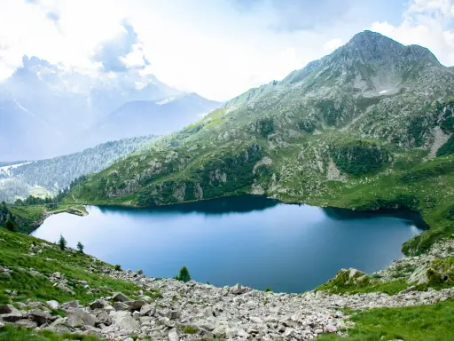 Un sereno lago ritorto incastonato tra montagne verdi e rocciose, con cime nebbiose all'orizzonte.
