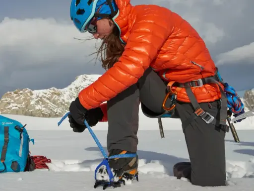 Alpinistka przygotowuje raki automatyczne lub półautomatyczne do wspinaczki. W tle góry.