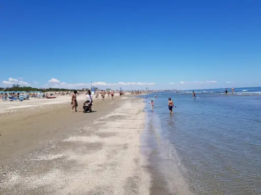 Una giornata di sole a Pinarella di Cervia mare, con bagnanti che passeggiano sulla sabbia e bambini che giocano nell'acqua cristallina.