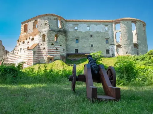 Zamek w Janowcu, ruiny z armatą na pierwszym planie, zielona trawa i błękitne niebo.
