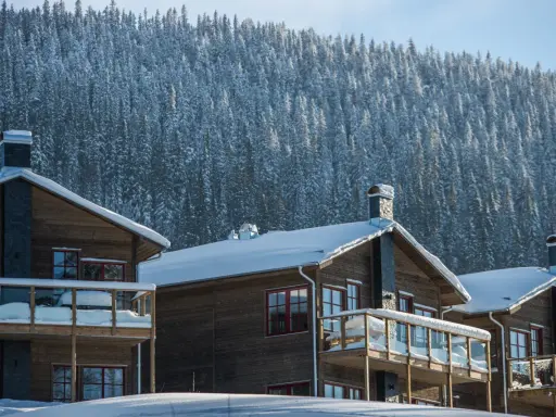 Vinteridyll vid STF Sylarna. Trähus med snötyngda tak och balkonger, mot en tät, snötäckt granskog.