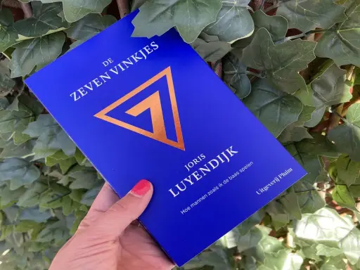 Blauwe kaft met gouden symbool en tekst "De Zeven Vinkjes" van Joris Luyendijk.