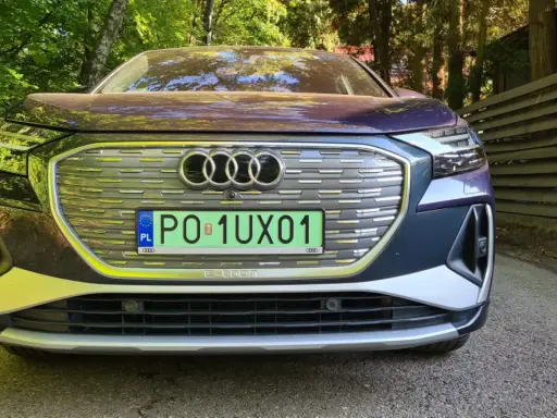 Elegancki, chromowany samochód Audi e-tron z polskimi tablicami rejestracyjnymi stoi na tle zielonego lasu.