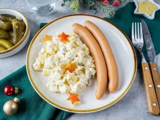 Kartoffelsalat mit Würstchen, dekoriert mit Sternen – ein Klassiker der 10 besten Weihnachtsessen. Dazu gibt es Gewürzgurken und Senf.