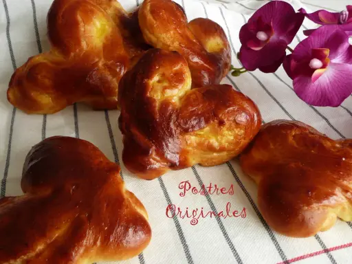 Pan de leche dorado y esponjoso, con forma de corazón, junto a orquídeas moradas. ¡Postres originales para disfrutar!
