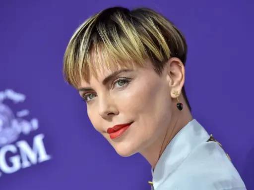 Charlize Theron mit fransigen Kurzhaarfrisuren Damen, rotem Lippenstift und Stern-Herz-Ohrringen vor MGM-Logo.