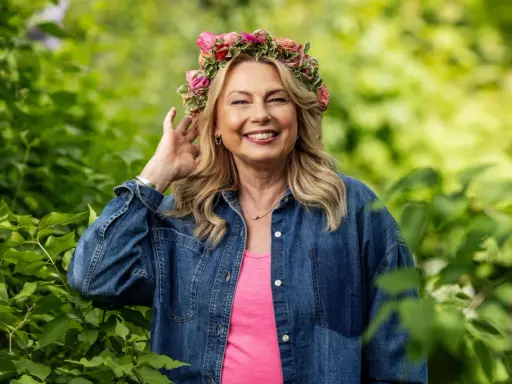 Glad kvinna med blomsterkrans ler i grönska. Hon är årets sommarpratare och bär jeansskjorta.